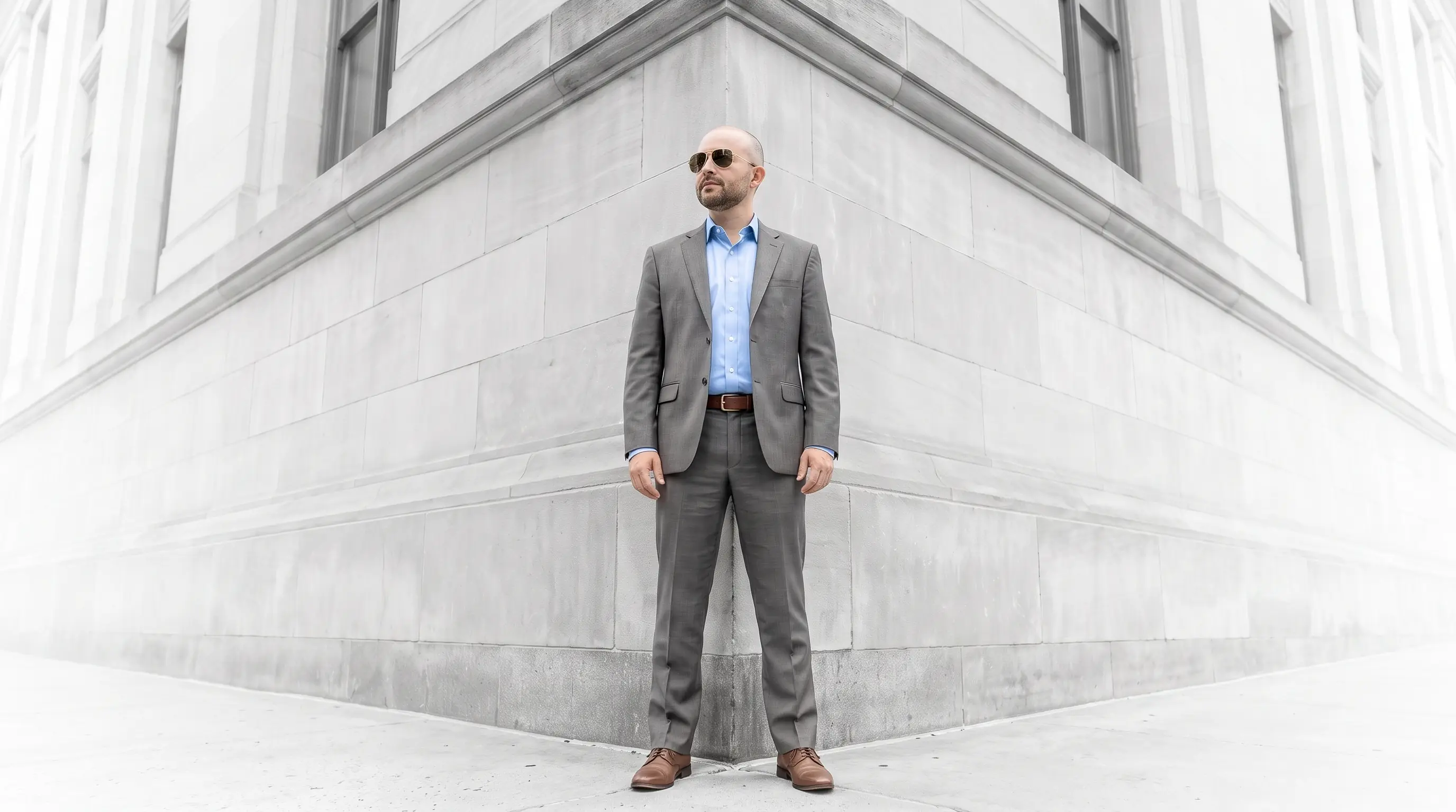 Ryan McEndarfer in a gray suit and light blue shirt, standing at the corner of a stone building